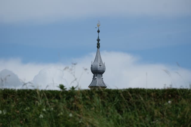 Onion-shaped church spire rising above a grassy hill under a blue sky with scattered clouds