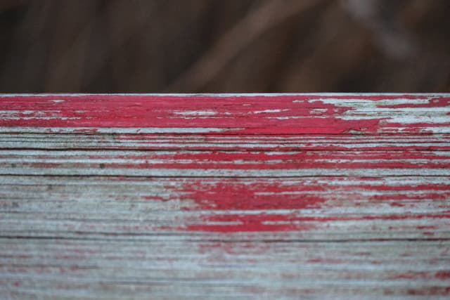 Close-up of distressed wooden boards with faded red paint and peeling, revealing gray wood grain