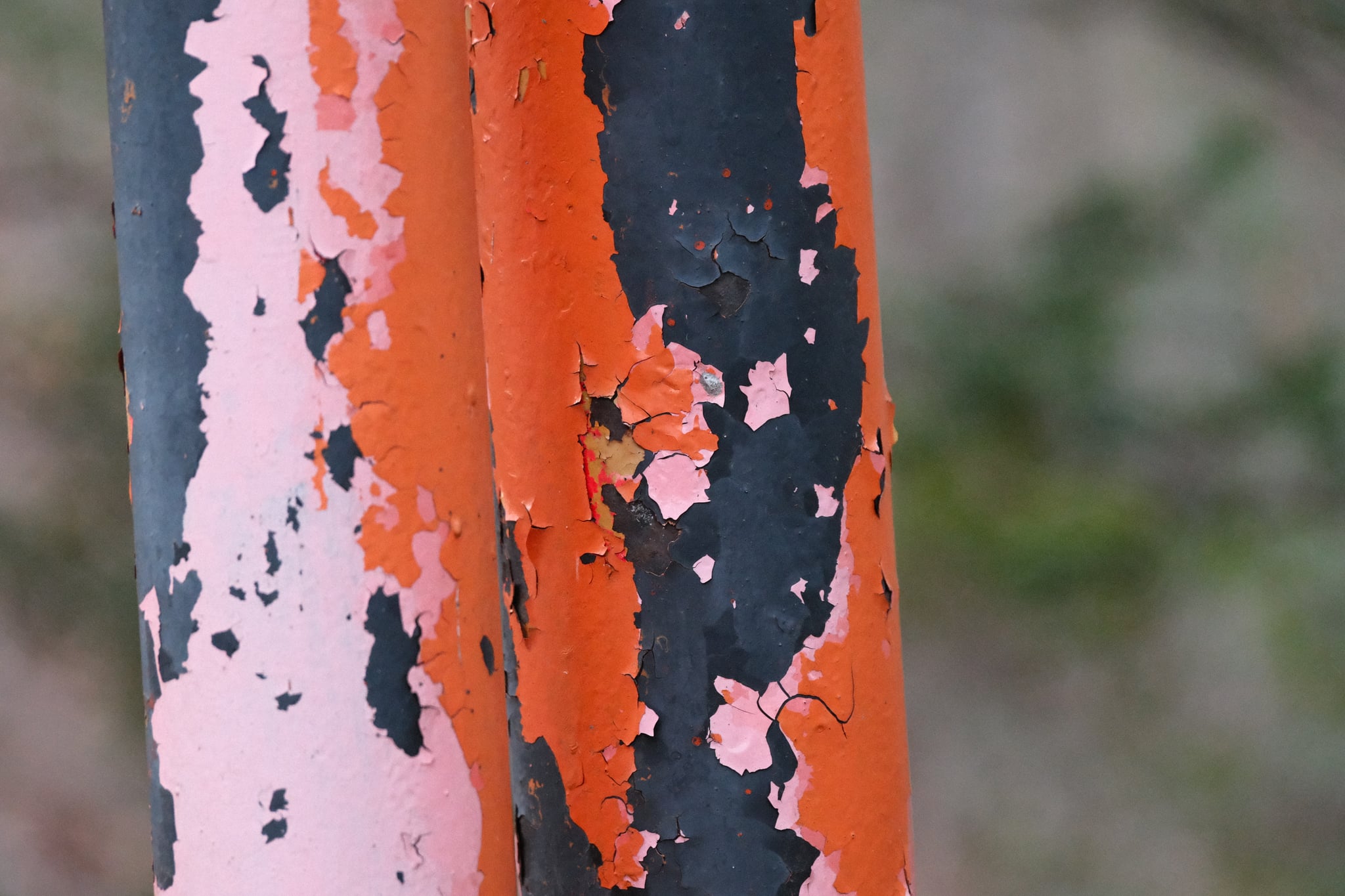 Close-up of weathered orange and black paint peeling off a metal pole with a blurred background