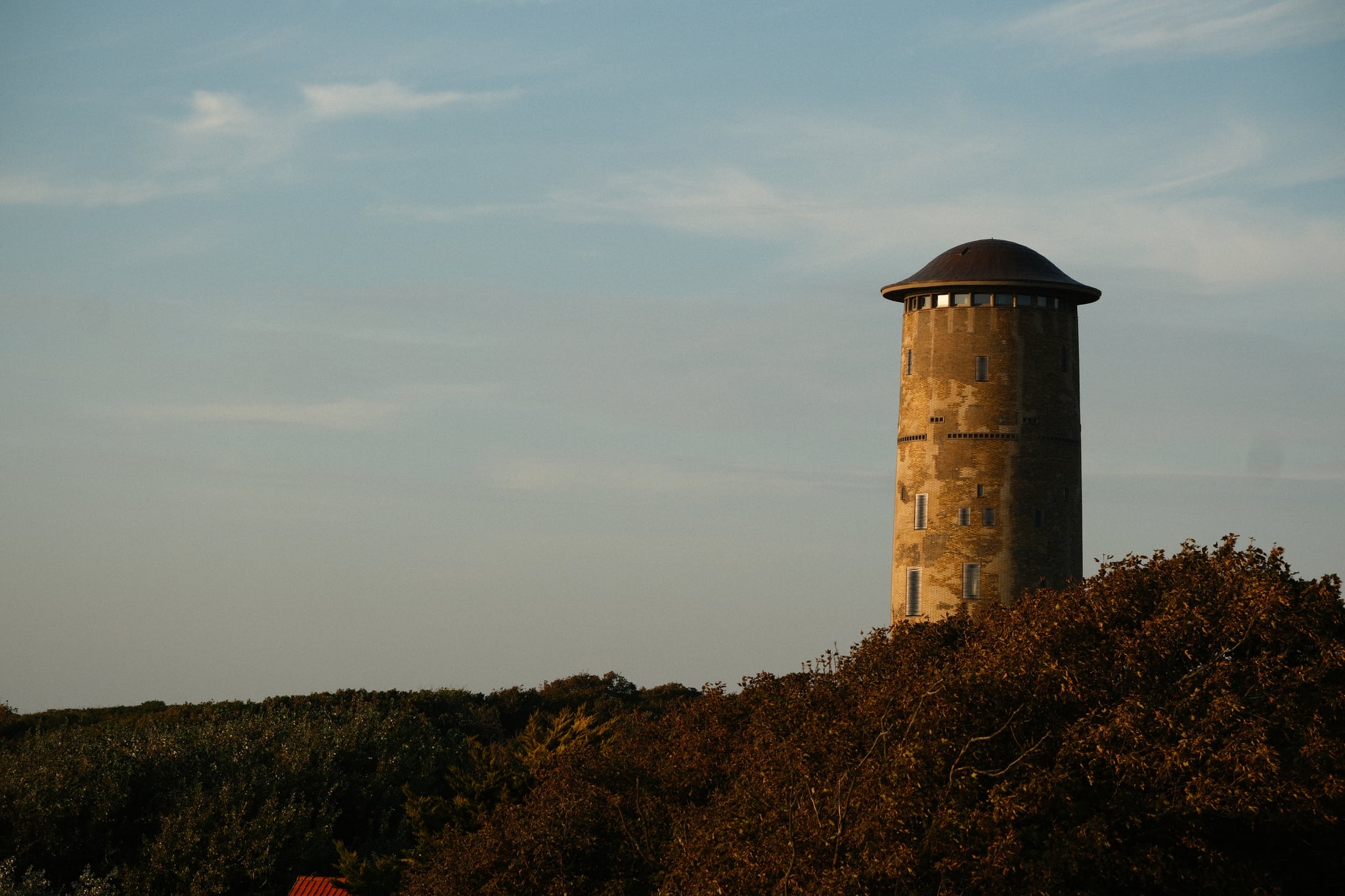 Cylindrical stone water tower standing above a tree-covered hillside under a pale sky