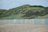 Sandy beach with a pastel-striped wooden fence in front of grassy dunes under a cloudy sky